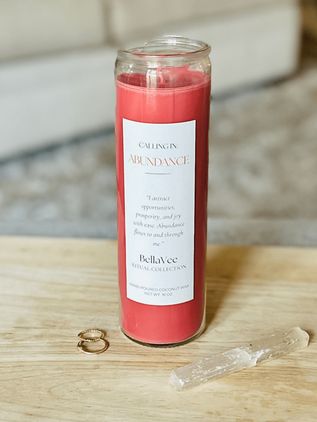The Abundance candle styled with rings and selenite on a wooden table, soft neutral background.