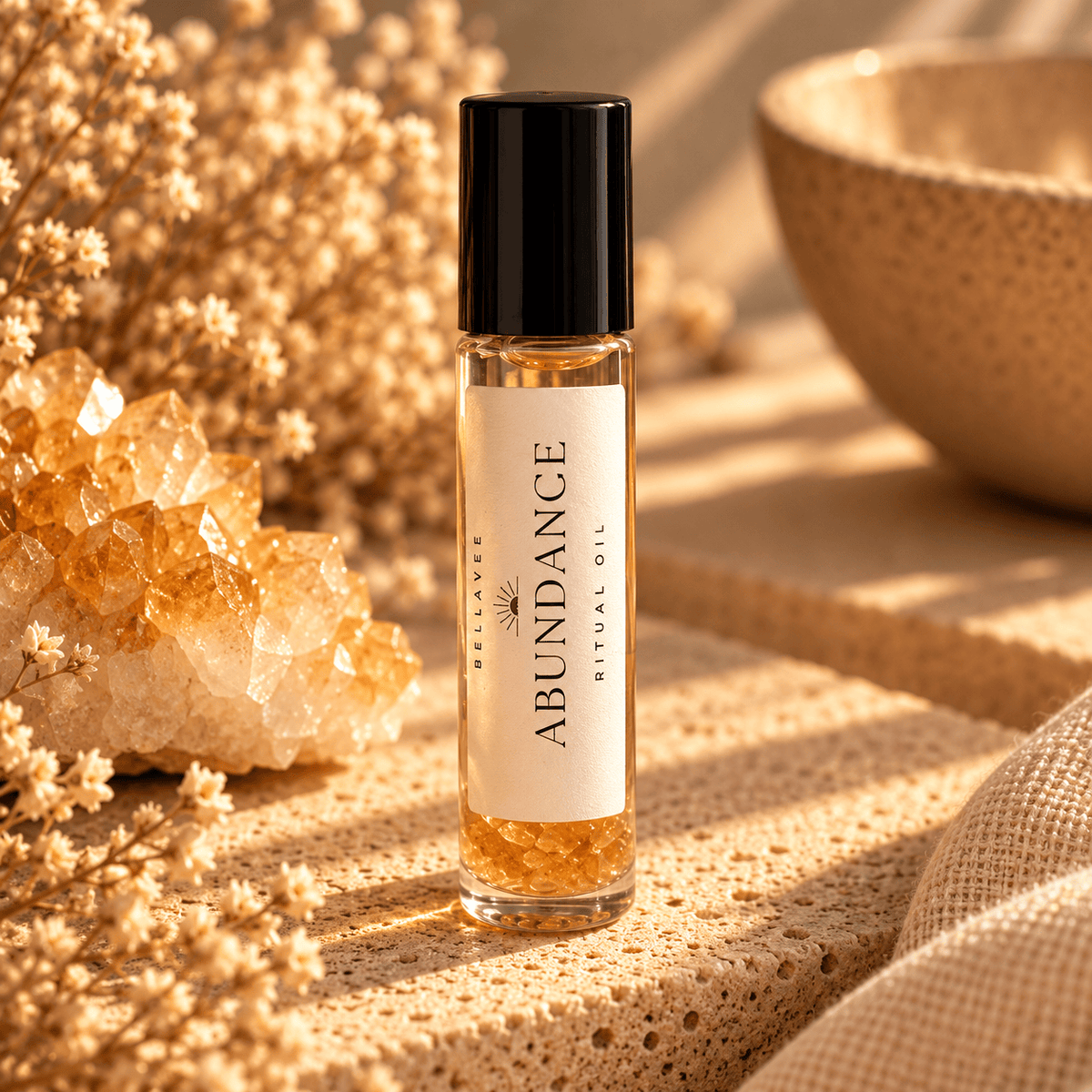 BellaVee ABUNDANCE Ritual Oil roll-on, displayed upright on natural stone with warm golden lighting and soft botanical accents.