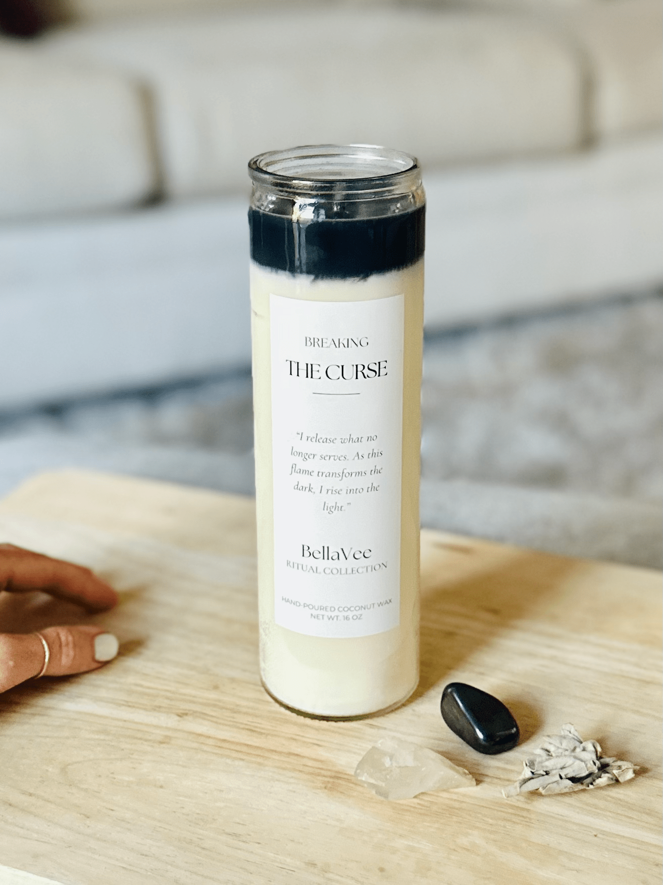The candle styled on a wooden surface with sage, black obsidian, and clear quartz.
