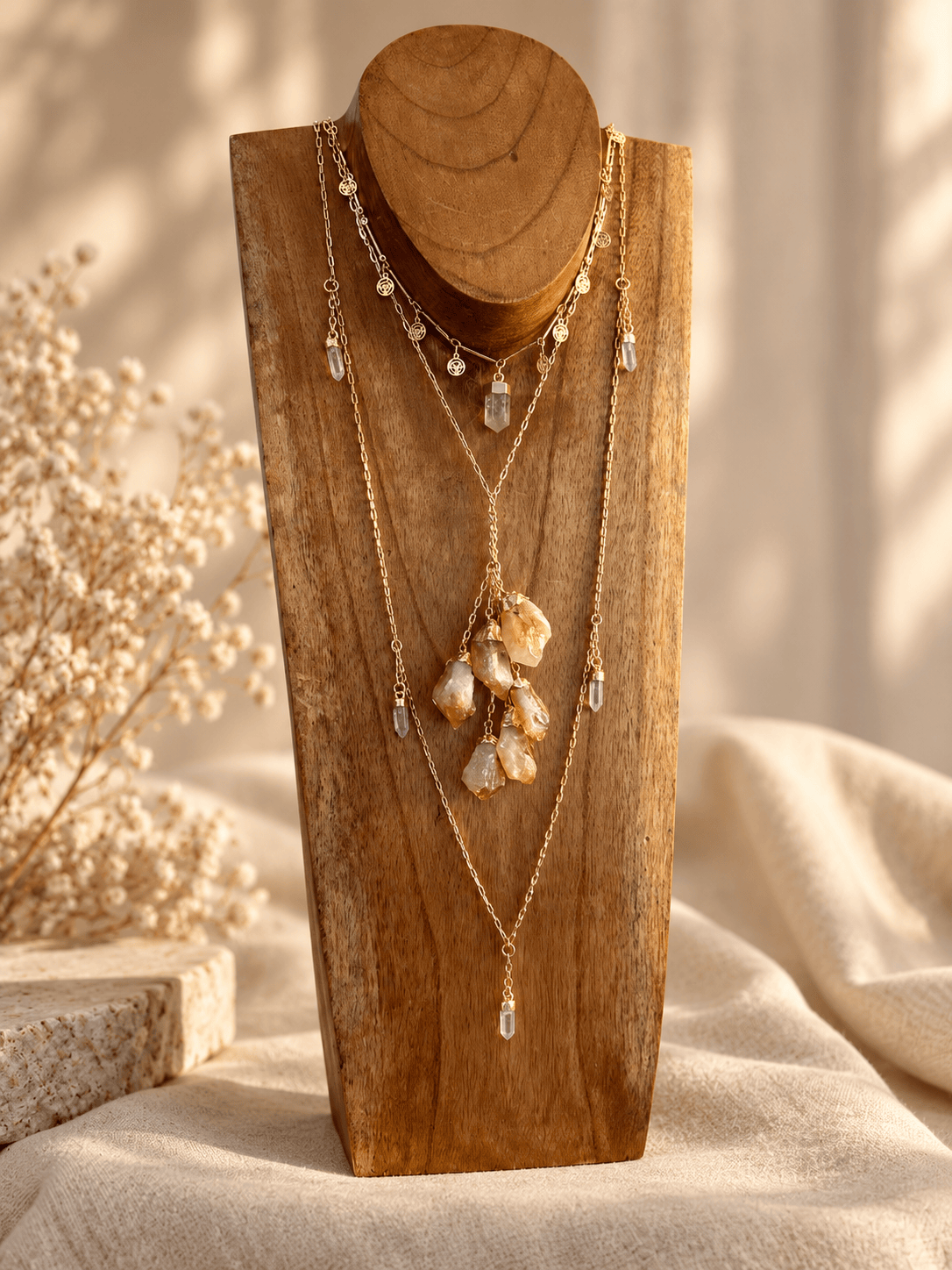 Citrine six-stone cluster drop necklace layered with gold crystal necklaces on wooden jewelry display