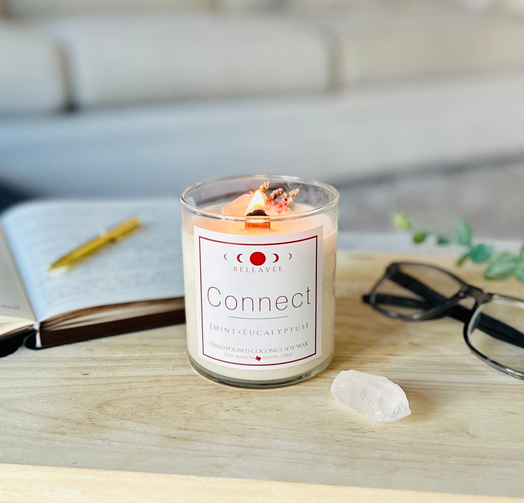 Lit Connect CBD Crystal Candle glowing with warm light, placed on a tabletop next to clear quartz and wellness items, evoking a calming aromatherapy ritual.