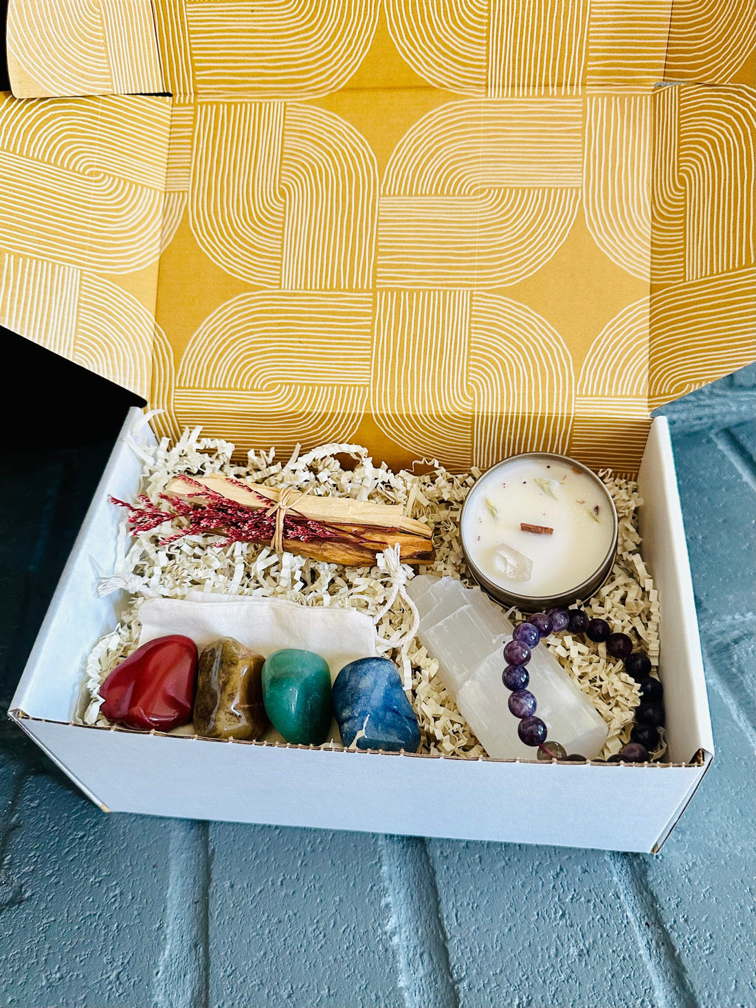 Holistic self-care gift box featuring crystal tumbles, Selenite Tower, Palo Santo, mini candle, and Amethyst bracelet for balance and positive energy.