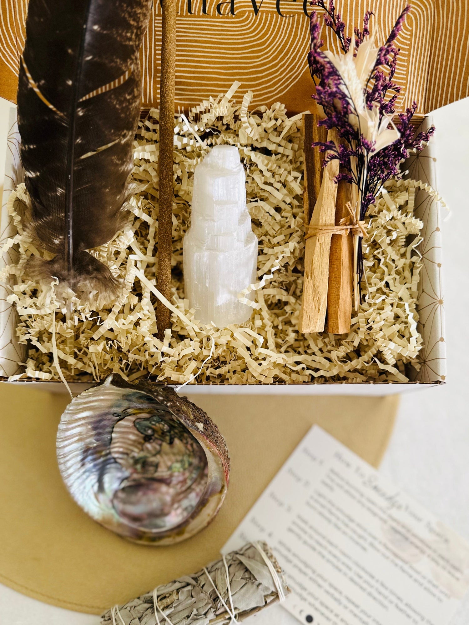 The BellaVee Smudge Kit contains a feather, abalone shell, hand-rolled Palo Santo incense, selenite tower, and sage or Palo Santo bundle