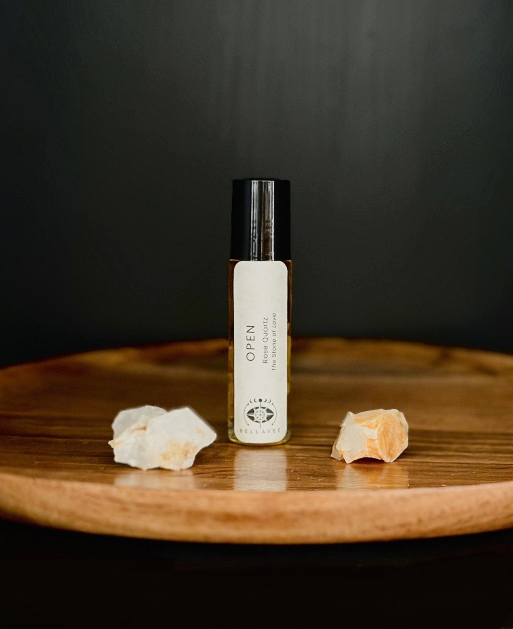 Crystal-infused essential oil roll-on labeled “Open” with Rose Quartz stones on a wooden surface.