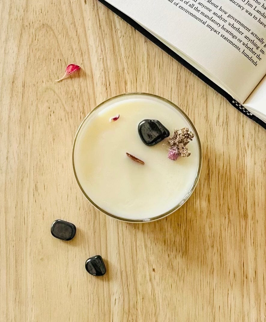 Top view of Integrity, Hematite Crystal candle topped with dries botanical and wooden wick, with a book and crystals surrounding it