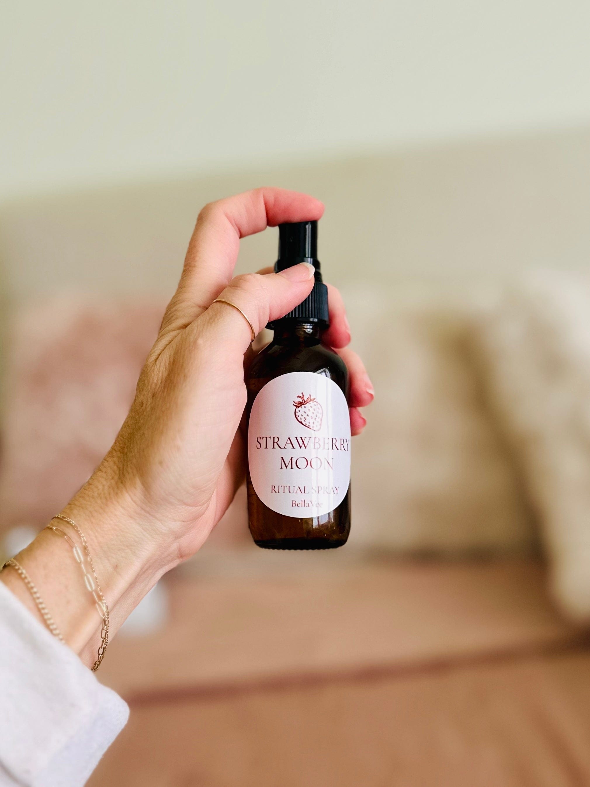 Hand holding aura spray ritual items on a soft pink background.