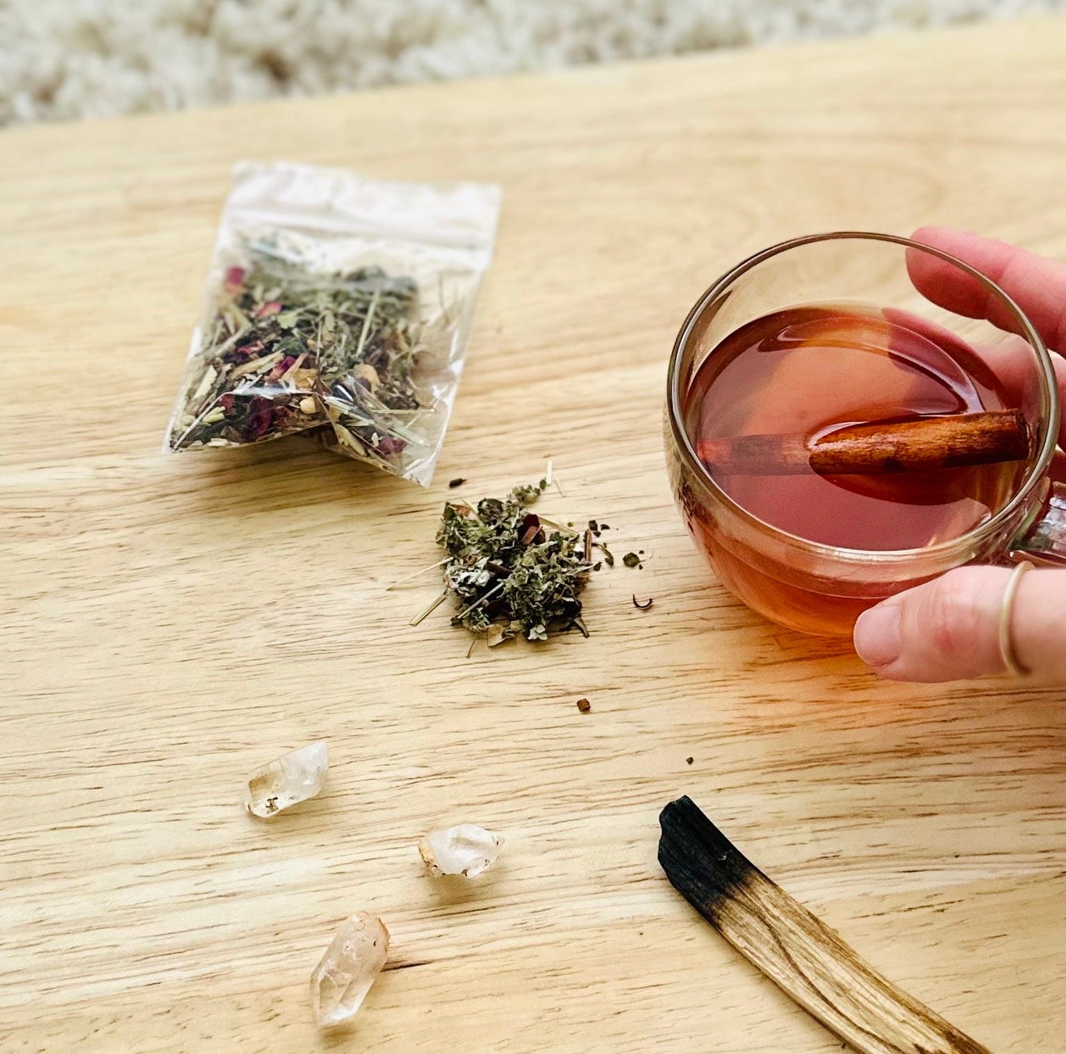 Hand holding moon tea near ritual items on a soft pink background.