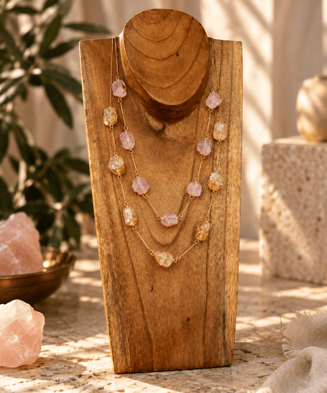 Rose Quartz and Citrine seven stone crystal necklaces on gold chains displayed on a wooden jewelry stand