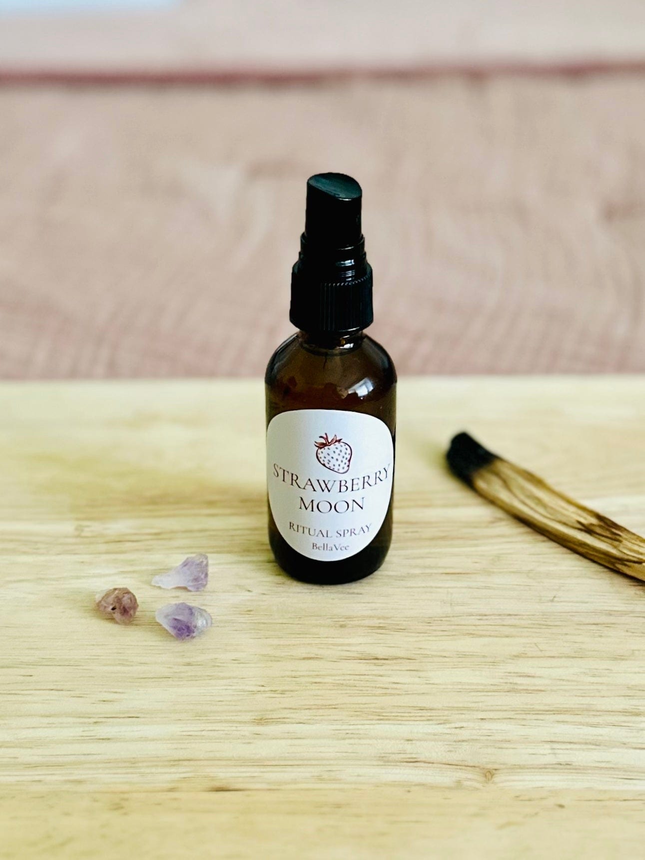 Close-up of BellaVee ritual spray bottle with crystals and Palo Santo nearby.