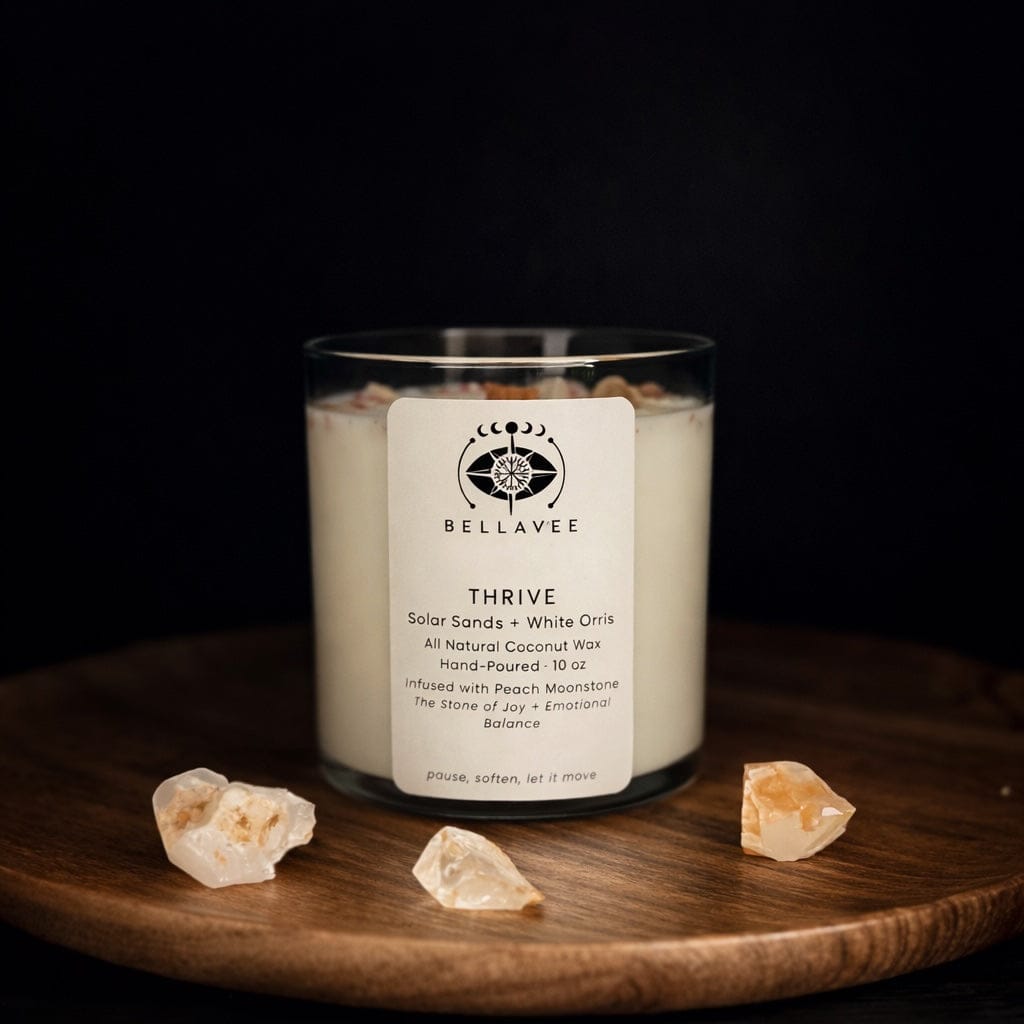 Thrive ritual candle made with coconut wax and peach moonstone, photographed on a wooden tray with natural stone accents in a moody setting.