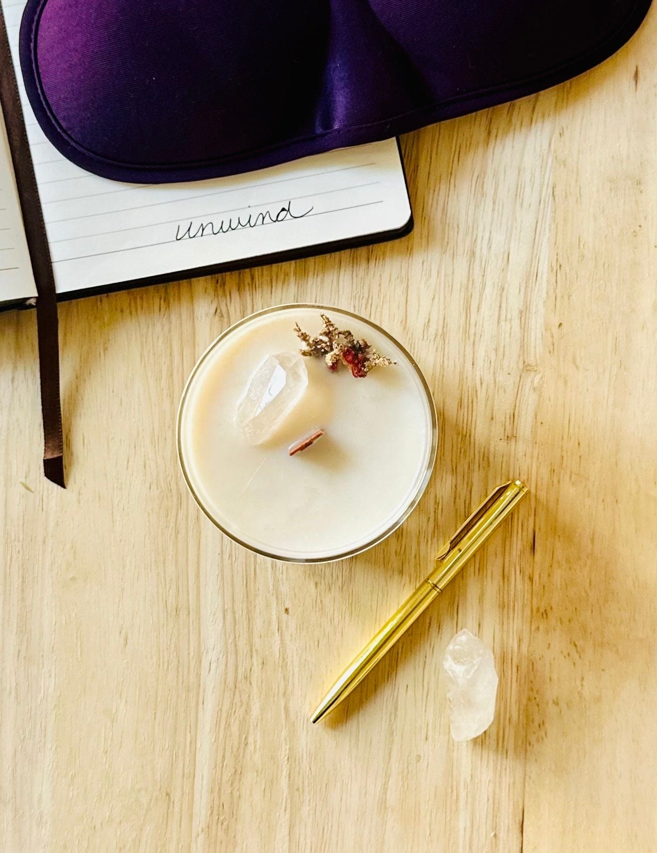 Top-down view of the Zen CBD Candle with wooden wick, topped with dried botanicals and a clear quartz crystal, showcasing handcrafted details and texture. with pen and notebook