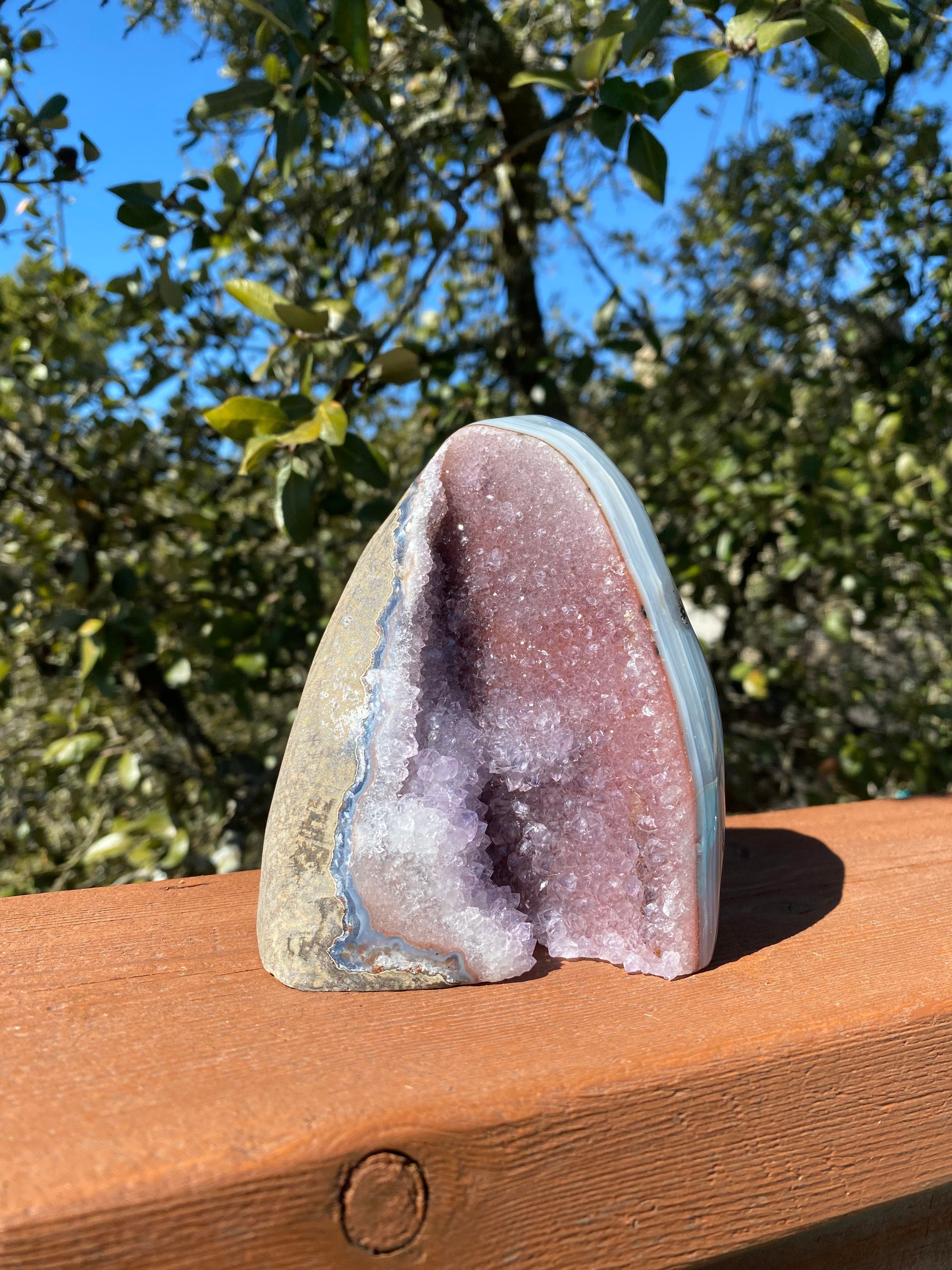 Under the sun, the Lavender Amethyst Geode glistens with vibrant purple crystals and stunning blue-white Brazilian Agate bands