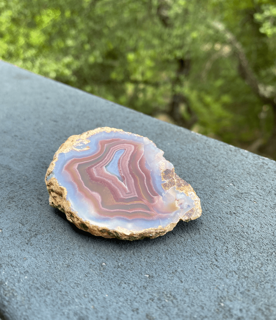 Cross-sectional Brazilian Agate slice with bands of blue, purple, gold, and rose, promoting harmony for the body, mind, and spirit.