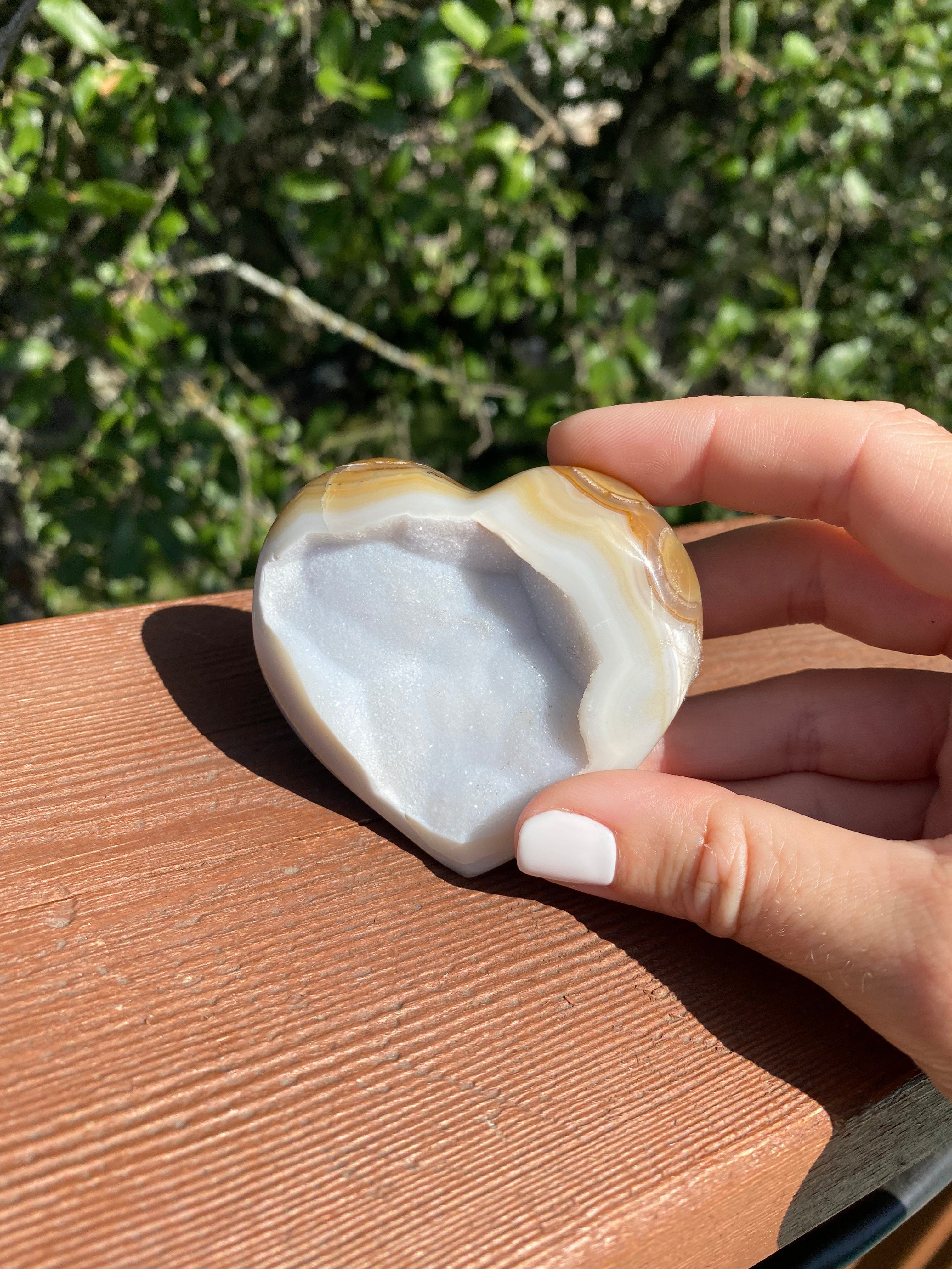 The Snow White Microcrystalline Agate Heart shines in hand, with intricate gold and cream bands and delicate glitter sparkling in the light