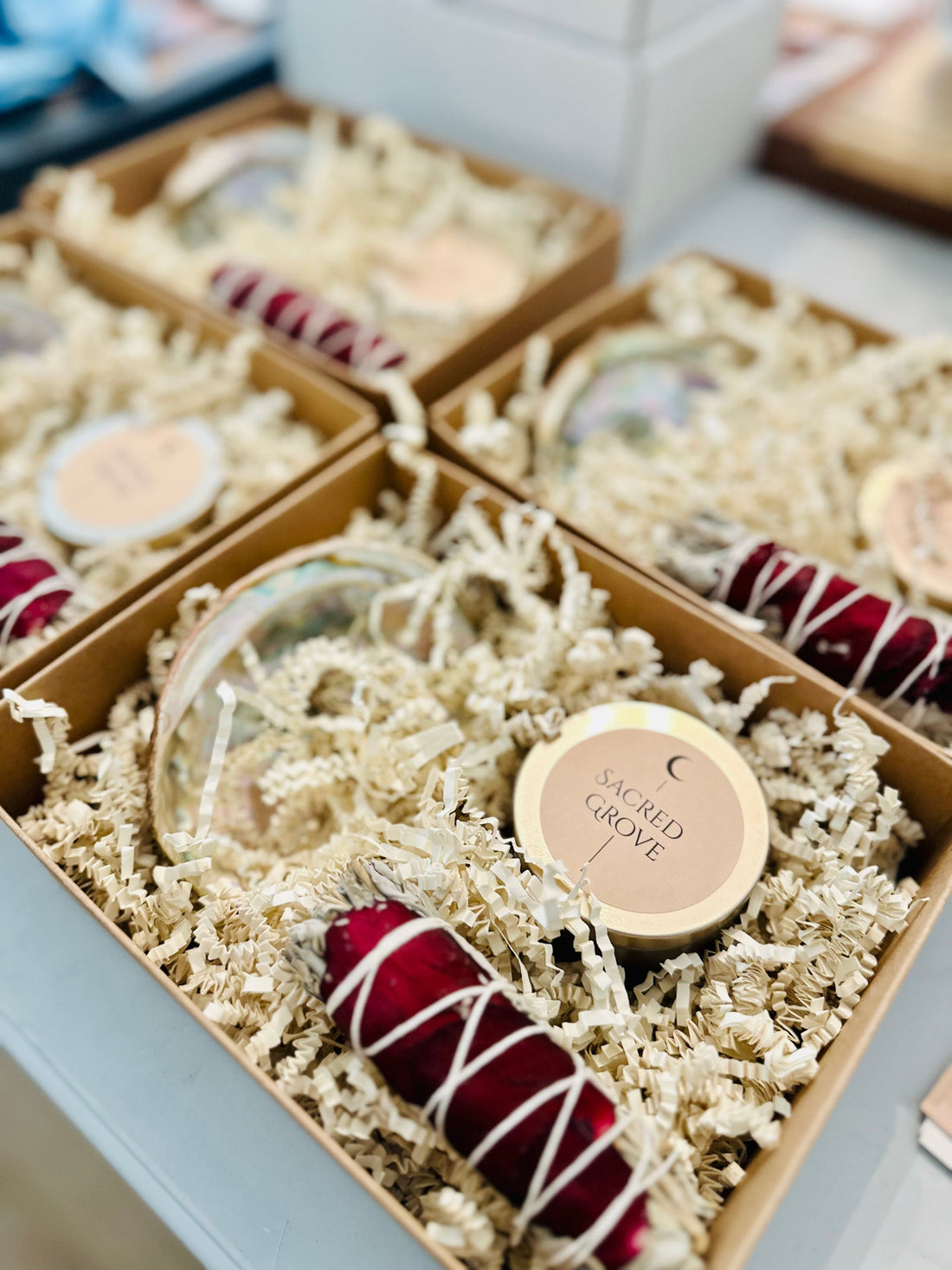 Mini ritual kits displayed in kraft boxes with shredded paper, including sage bundles, mini candles, and abalone shells.