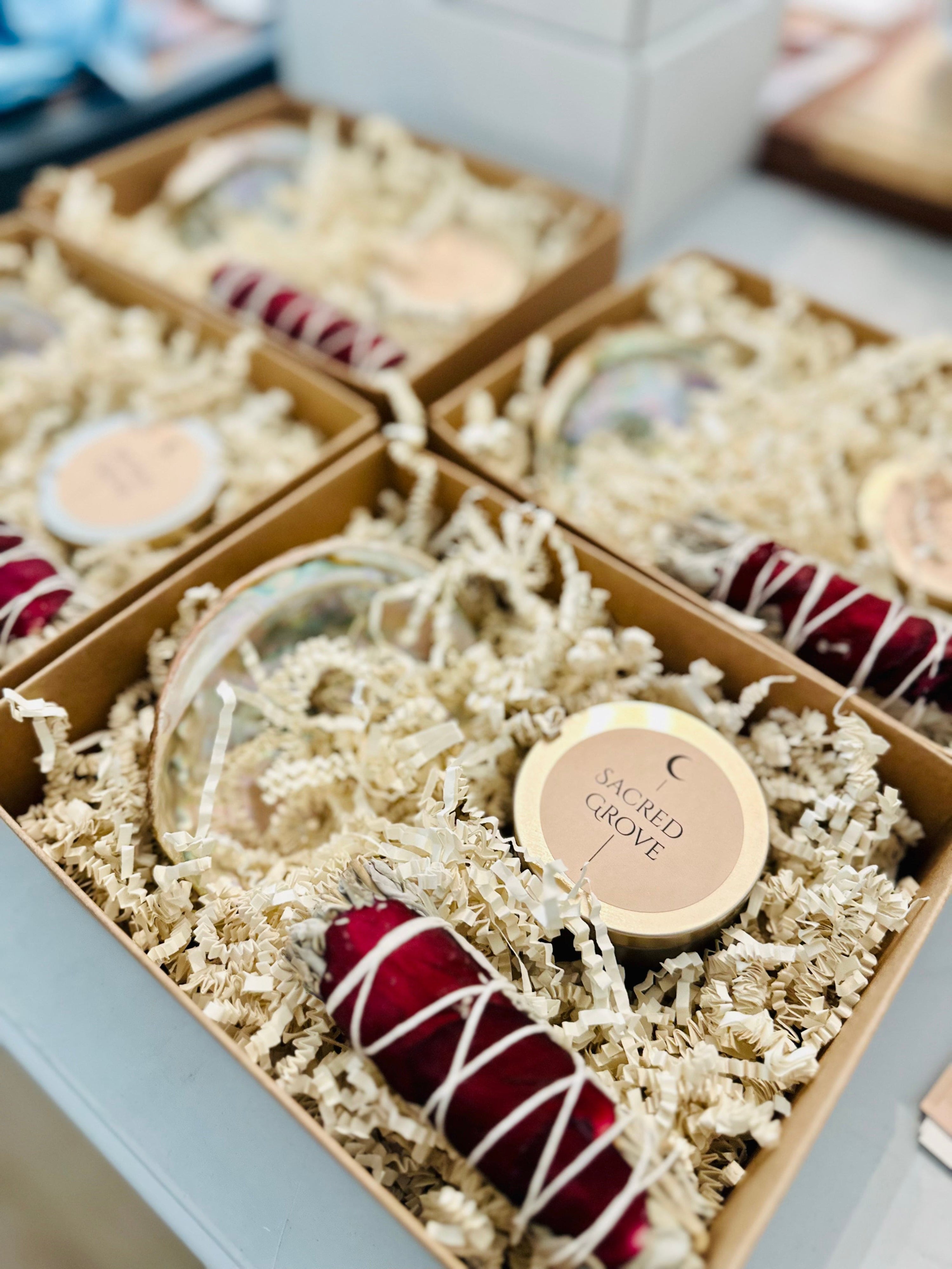 Mini ritual kits displayed in kraft boxes with shredded paper, including sage bundles, mini candles, and abalone shells.