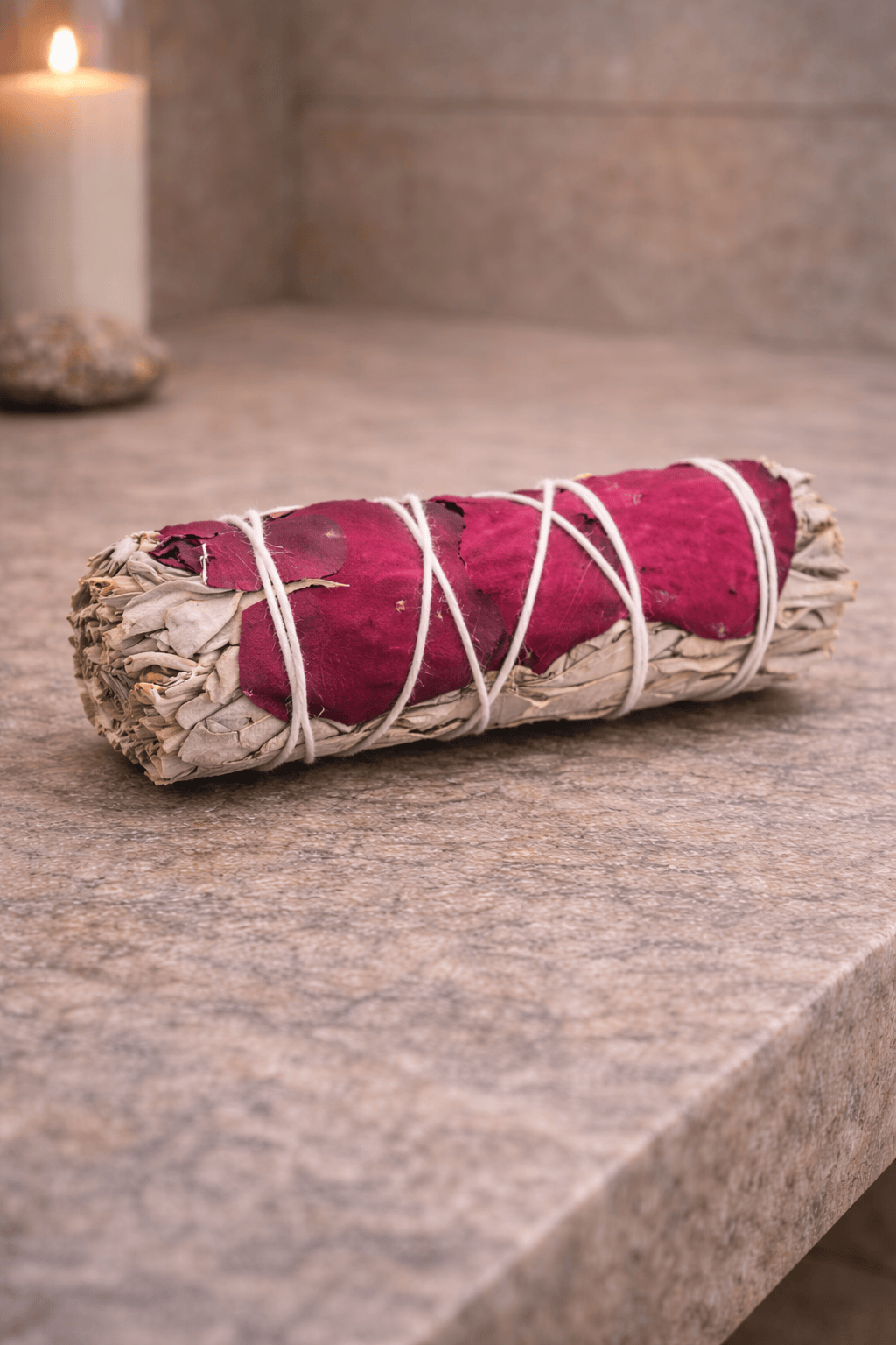 Rolled sage bundle with red fabric on a wooden surface, candle in the background