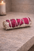 Rolled sage bundle with red fabric on a wooden surface, candle in the background