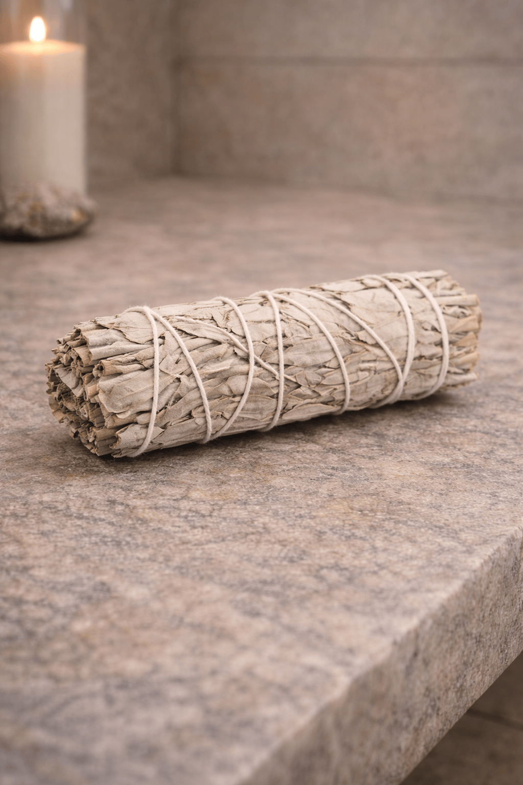 Rolled sage smudge stick on a stone surface with a blurred candle in the background