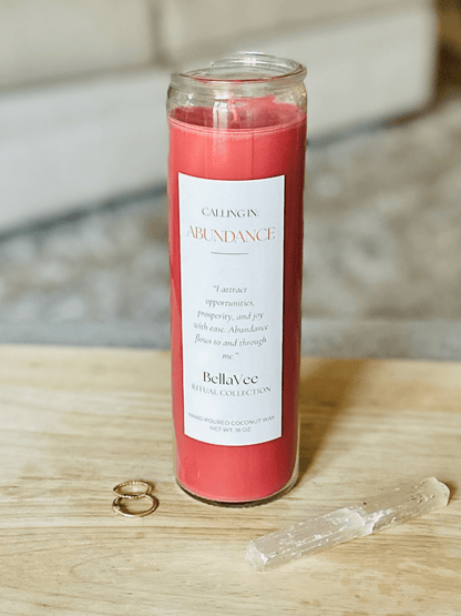 The Abundance candle styled with rings and selenite on a wooden table, soft neutral background.