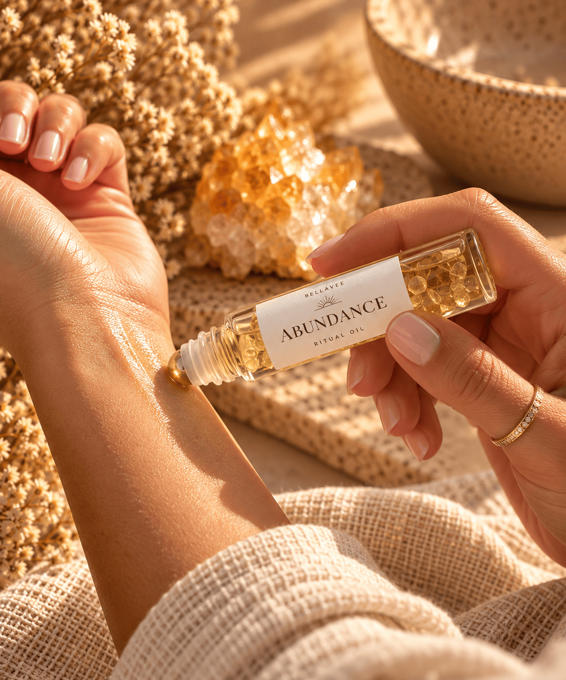 Woman applying BellaVee ABUNDANCE Ritual Oil to her wrist during a mindful self-care ritual, with soft natural lighting and warm neutral tones.