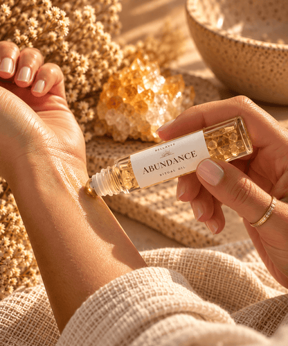 Woman applying BellaVee ABUNDANCE Ritual Oil to her wrist during a mindful self-care ritual, with soft natural lighting and warm neutral tones.