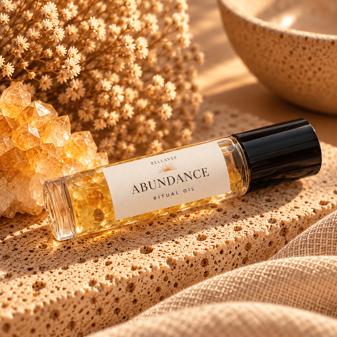 BellaVee ABUNDANCE Ritual Oil roll-on, displayed upright on natural stone with warm golden lighting and soft botanical accents.