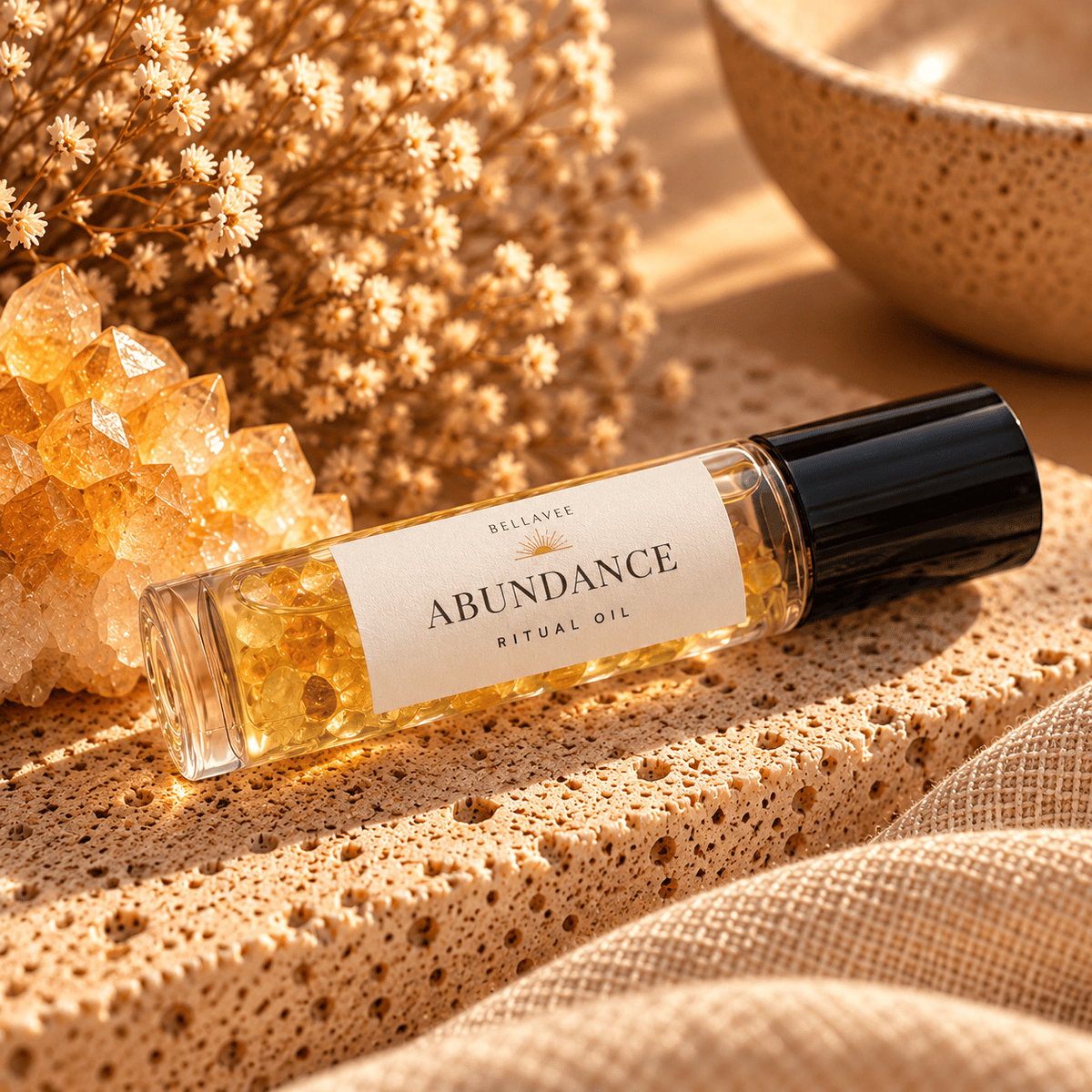 BellaVee ABUNDANCE Ritual Oil roll-on, displayed upright on natural stone with warm golden lighting and soft botanical accents.