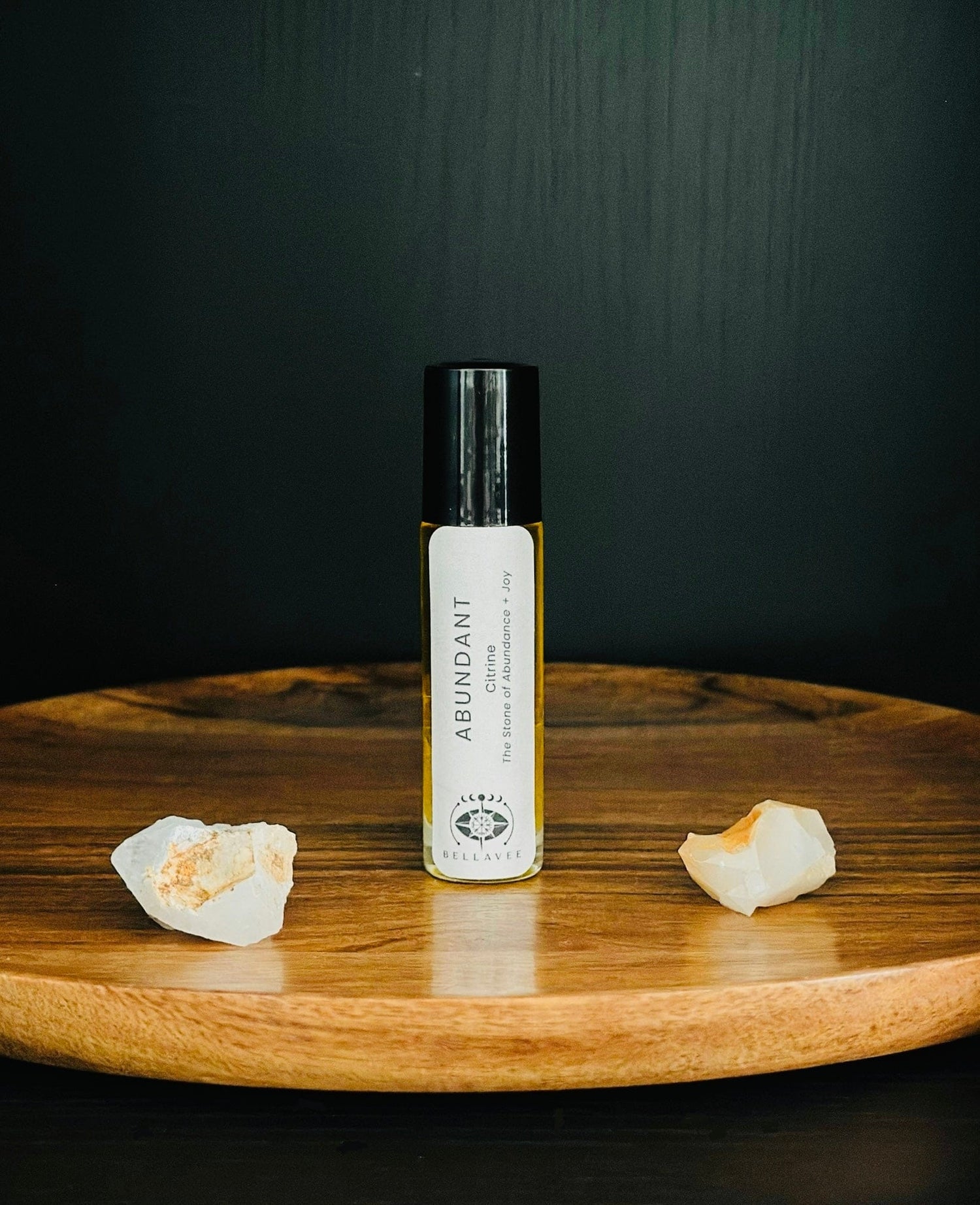 Crystal-infused essential oil roll-on labeled “Abundant” with Citrine stones on a wooden tray.
