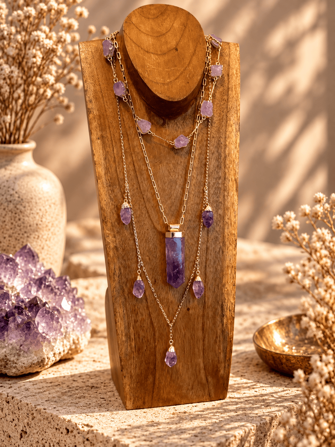 Amethyst crystal pendant necklace layered with gold crystal jewelry on a wooden jewelry stand