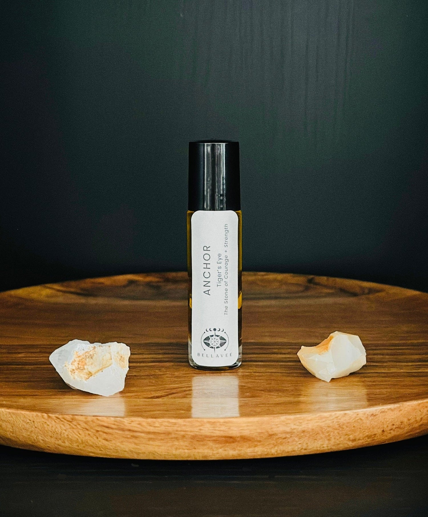 Crystal-infused essential oil roll-on labeled “Anchor” with Tiger’s Eye stones on a wooden surface.