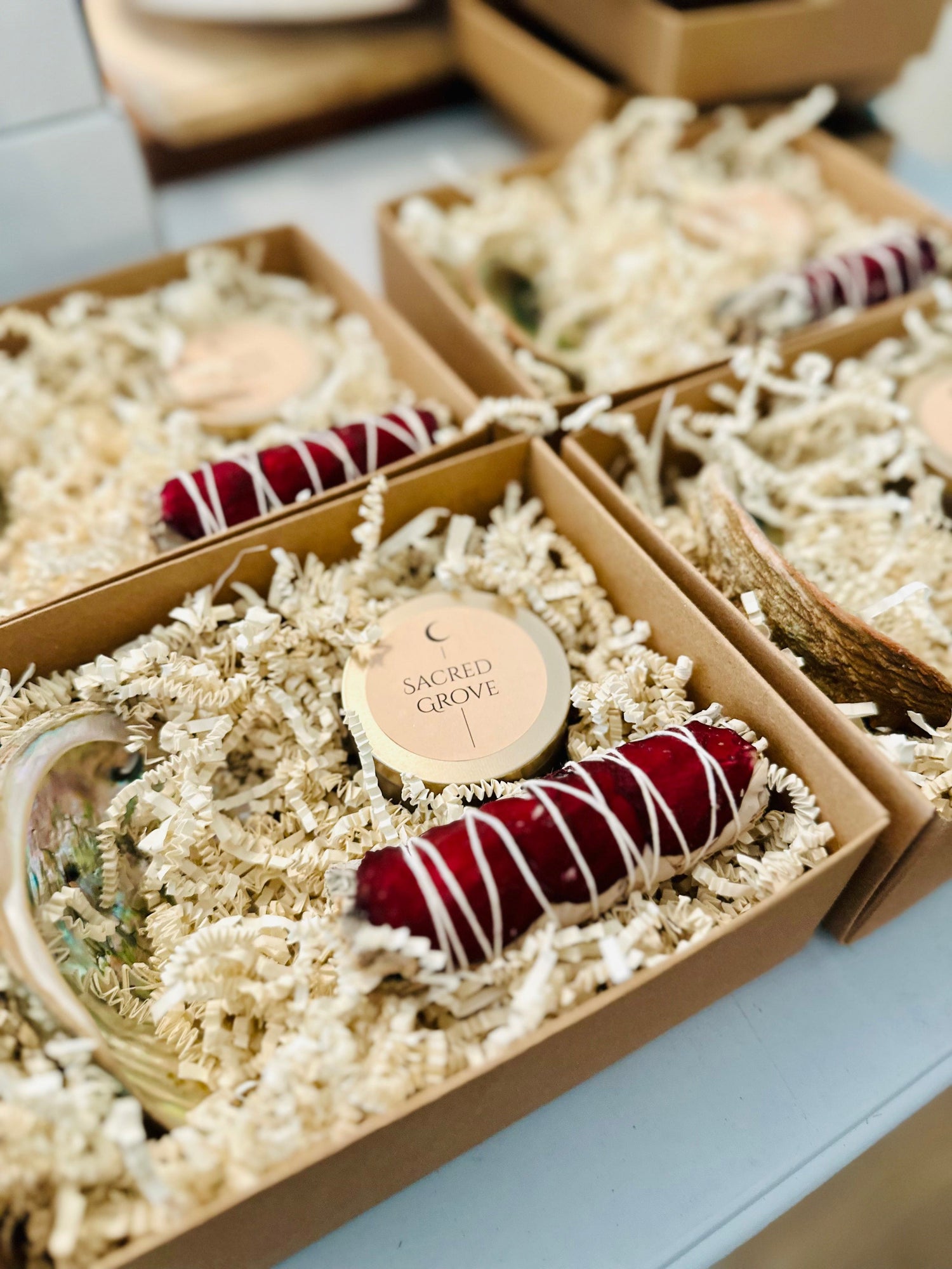 Close-up of a Sacred Grove candle with a deep red sage bundle and black obsidian tower nestled in a gift box.