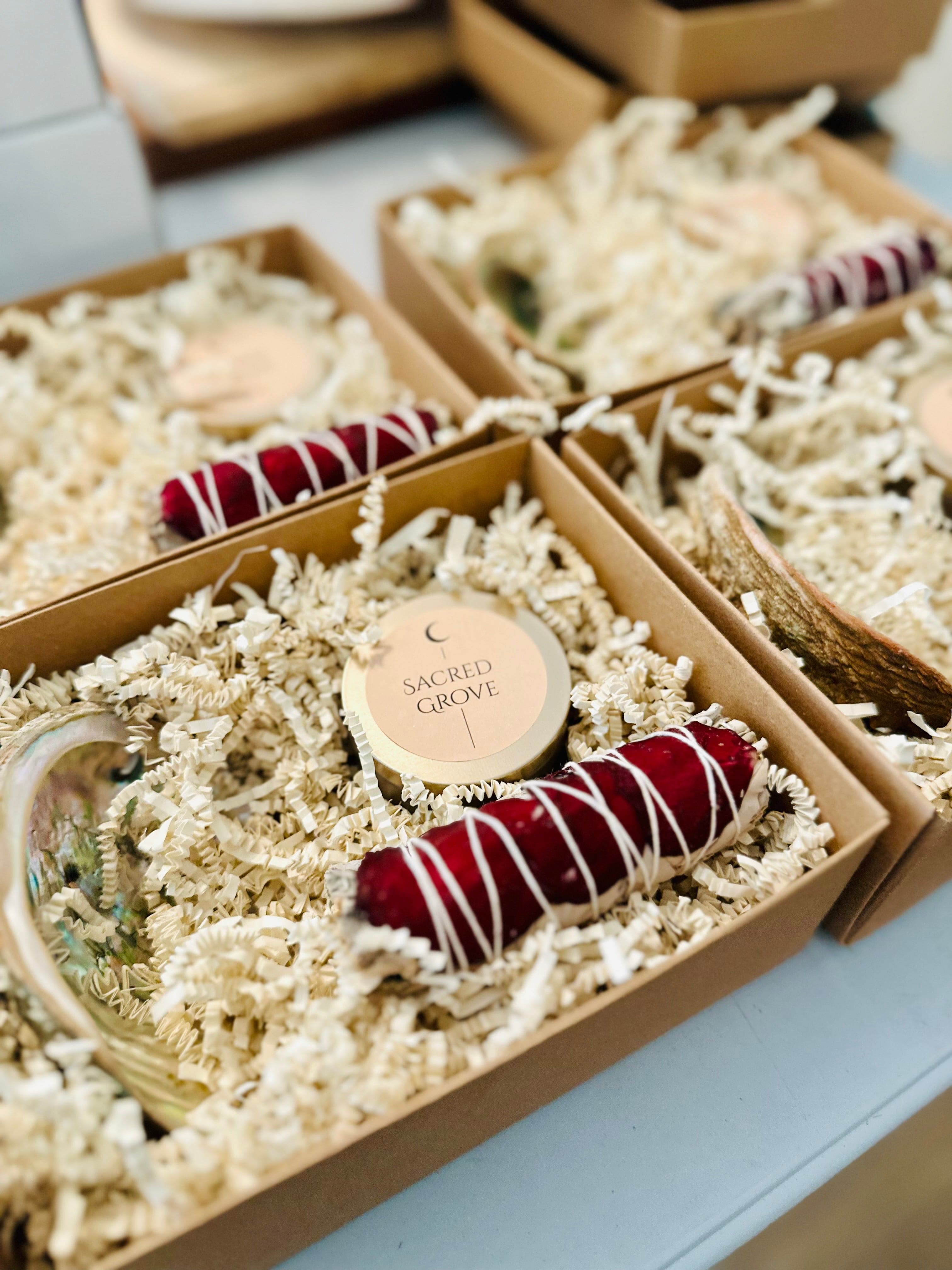 Close-up of a Sacred Grove candle with a deep red sage bundle and black obsidian tower nestled in a gift box.