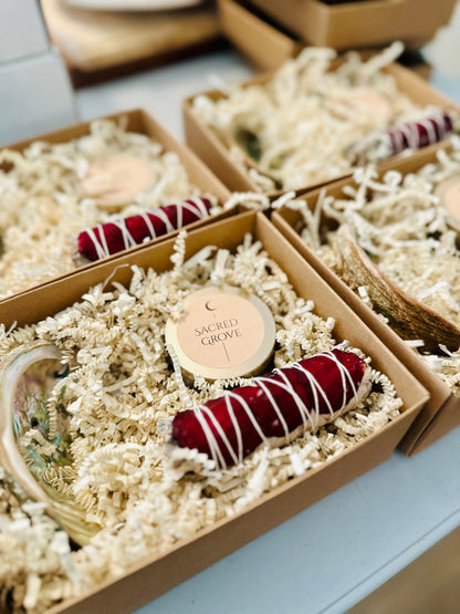 Close-up of a Sacred Grove candle with a deep red sage bundle and black obsidian tower nestled in a gift box.