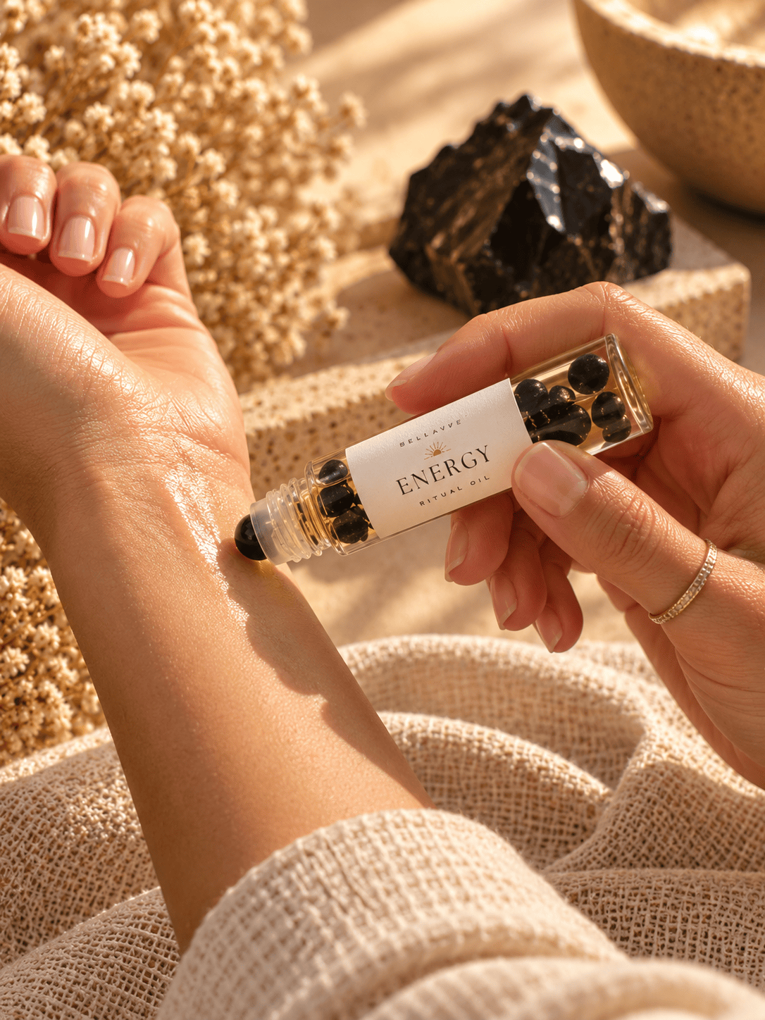 Woman applying BellaVee ENERGY Ritual Oil with black obsidian chips to her wrist during a calming self-care ritual.