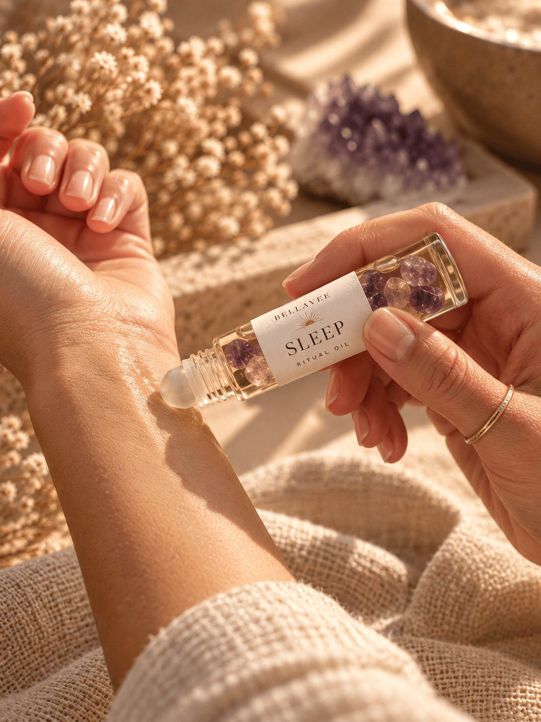 Woman applying BellaVee SLEEP Ritual Oil infused with amethyst chips to her wrist during a relaxing bedtime self-care ritual.