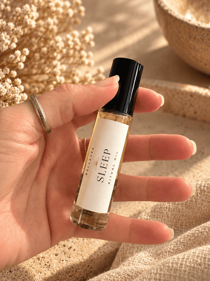 Close-up of a woman holding BellaVee SLEEP Ritual Oil roll-on against a warm, neutral background with soft natural lighting.