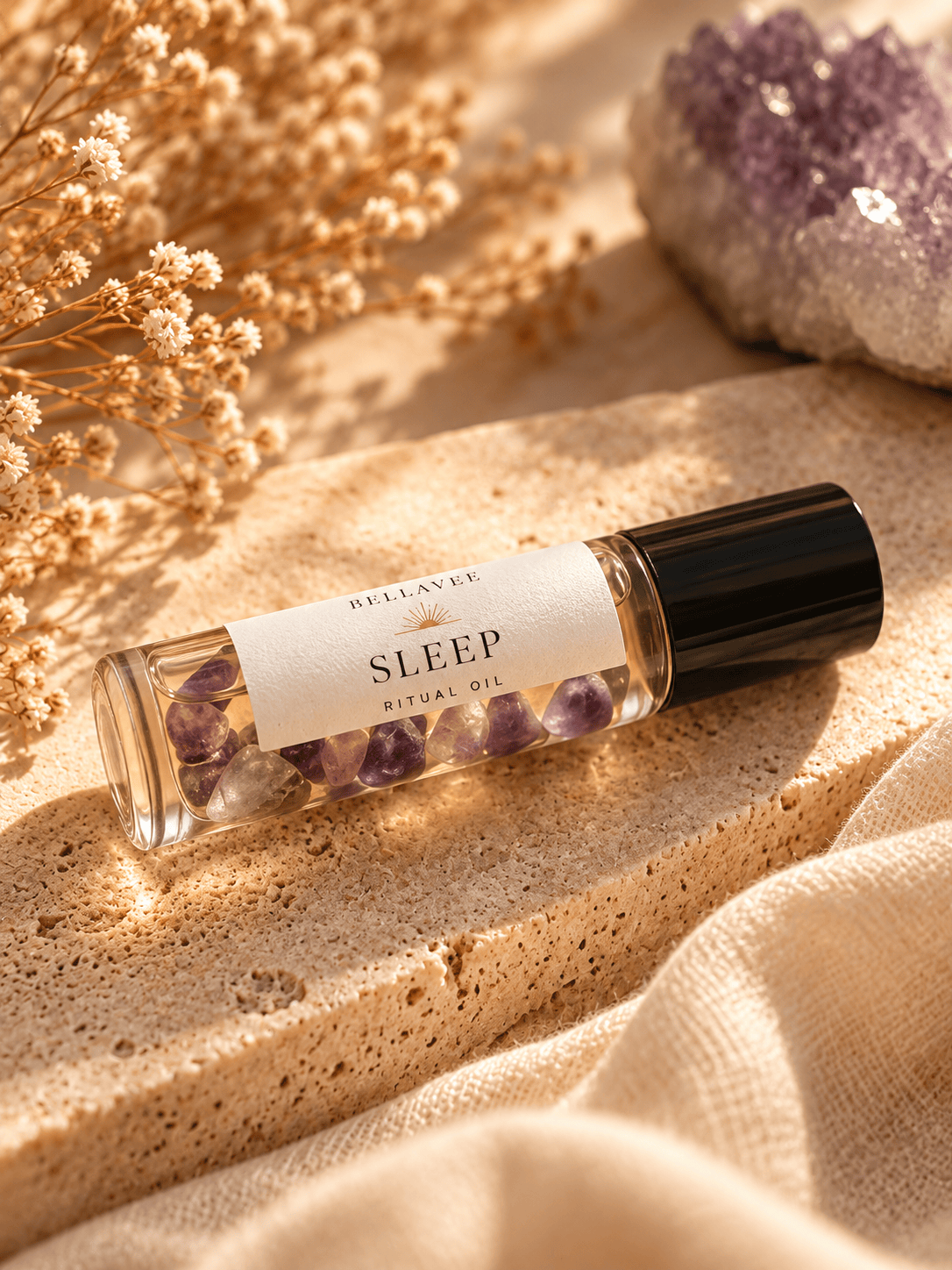 BellaVee SLEEP Ritual Oil roll-on with amethyst chips, displayed upright on natural stone with warm golden lighting and soft botanical accents.