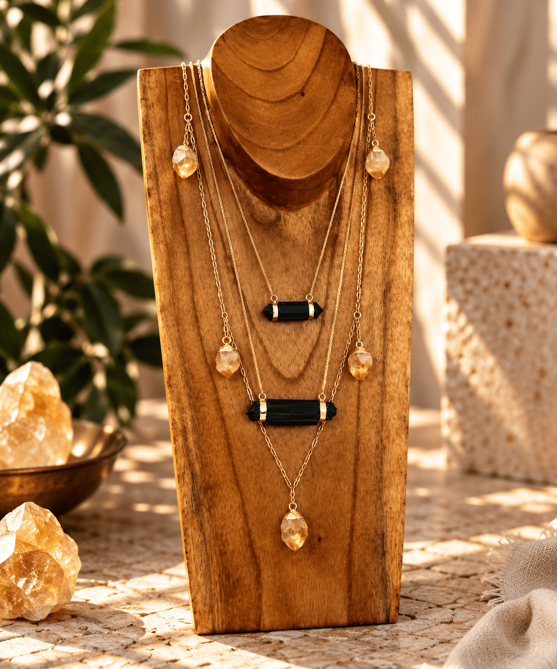 Raw Black Tourmaline bar necklace layered with gold crystal necklaces on a wooden jewelry stand