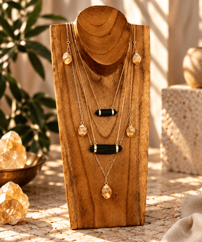 Raw Black Tourmaline bar necklace layered with gold crystal necklaces on a wooden jewelry stand