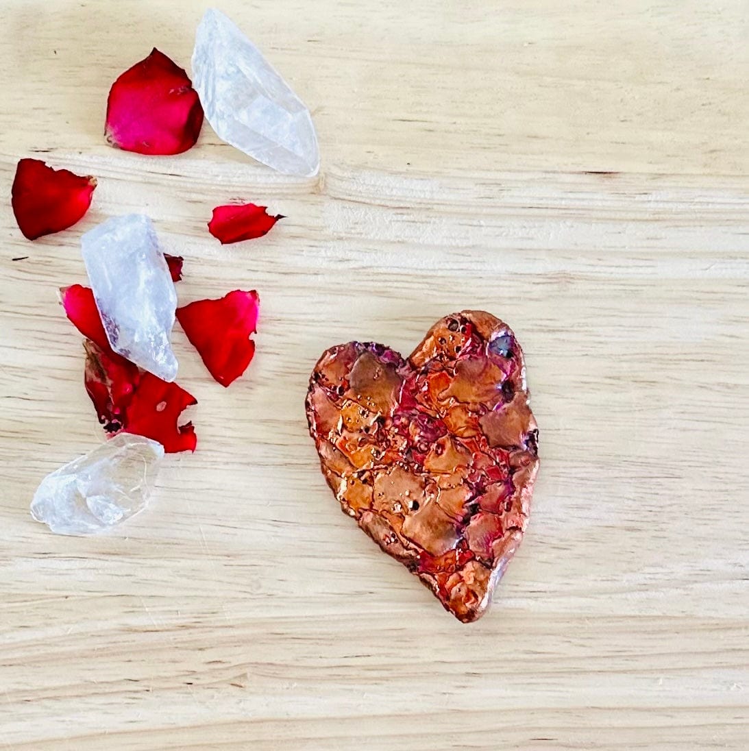 Close-up of copper heart showing natural splash texture and patina, with petals and crystals surrounding it