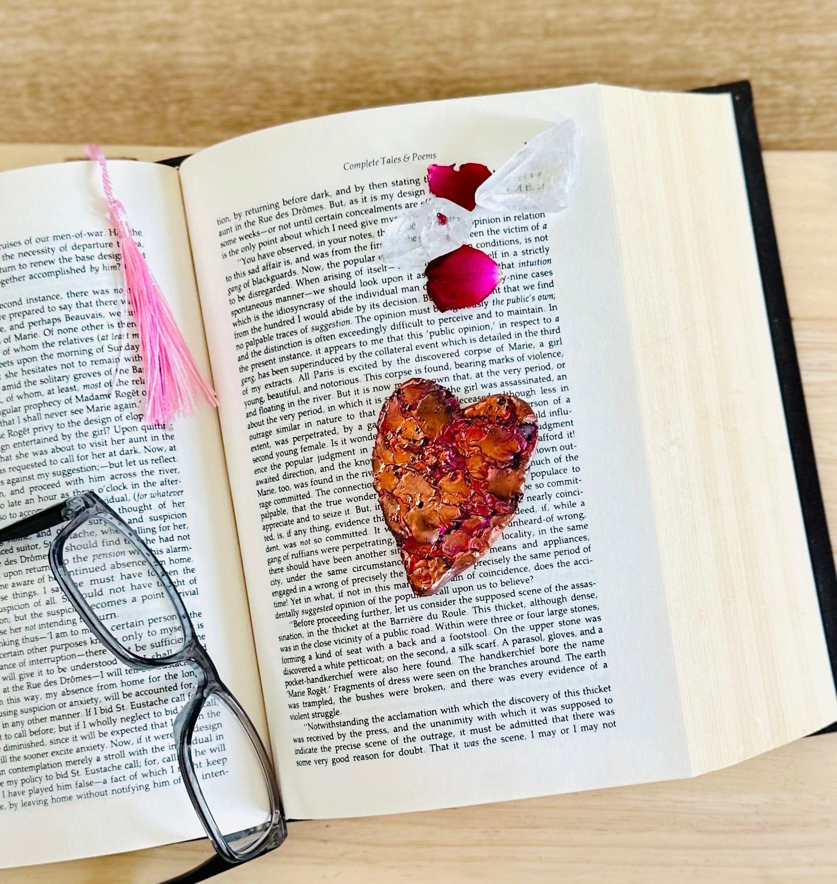 Flat lay of Copper heart on book, with rose petals and crystals for a warm vibe.

