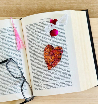 Flat lay of Copper heart on book, with rose petals and crystals for a warm vibe.
