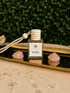OY non-toxic car diffuser by BellaVee, glass bottle with wood cap and hanging rope, styled with rose quartz on a mirrored tray