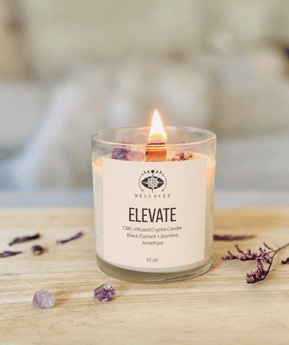 BellaVee ELEVATE CBD-infused crystal candle with black currant and jasmine fragrance, amethyst crystal, and wooden wick burning in a calming home setting.