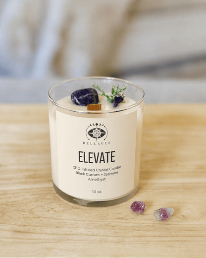BellaVee ELEVATE CBD crystal candle featuring black currant and jasmine scent, amethyst crystal, botanical accents, and a wooden wick in a clear glass vessel.