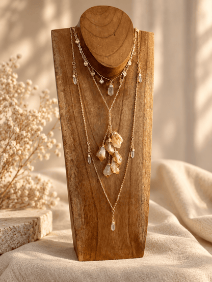 Seven-stone Clear Quartz necklace layered with gold crystal jewelry on wooden display