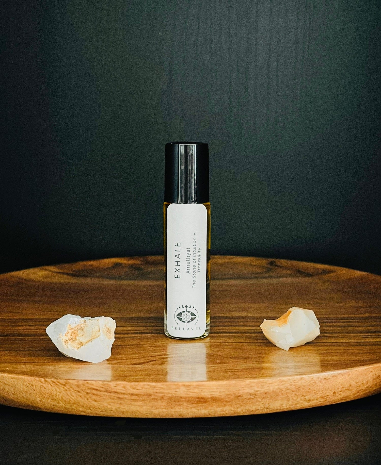 Crystal-infused essential oil roll-on labeled “Exhale” with Amethyst stones on a wooden surface.