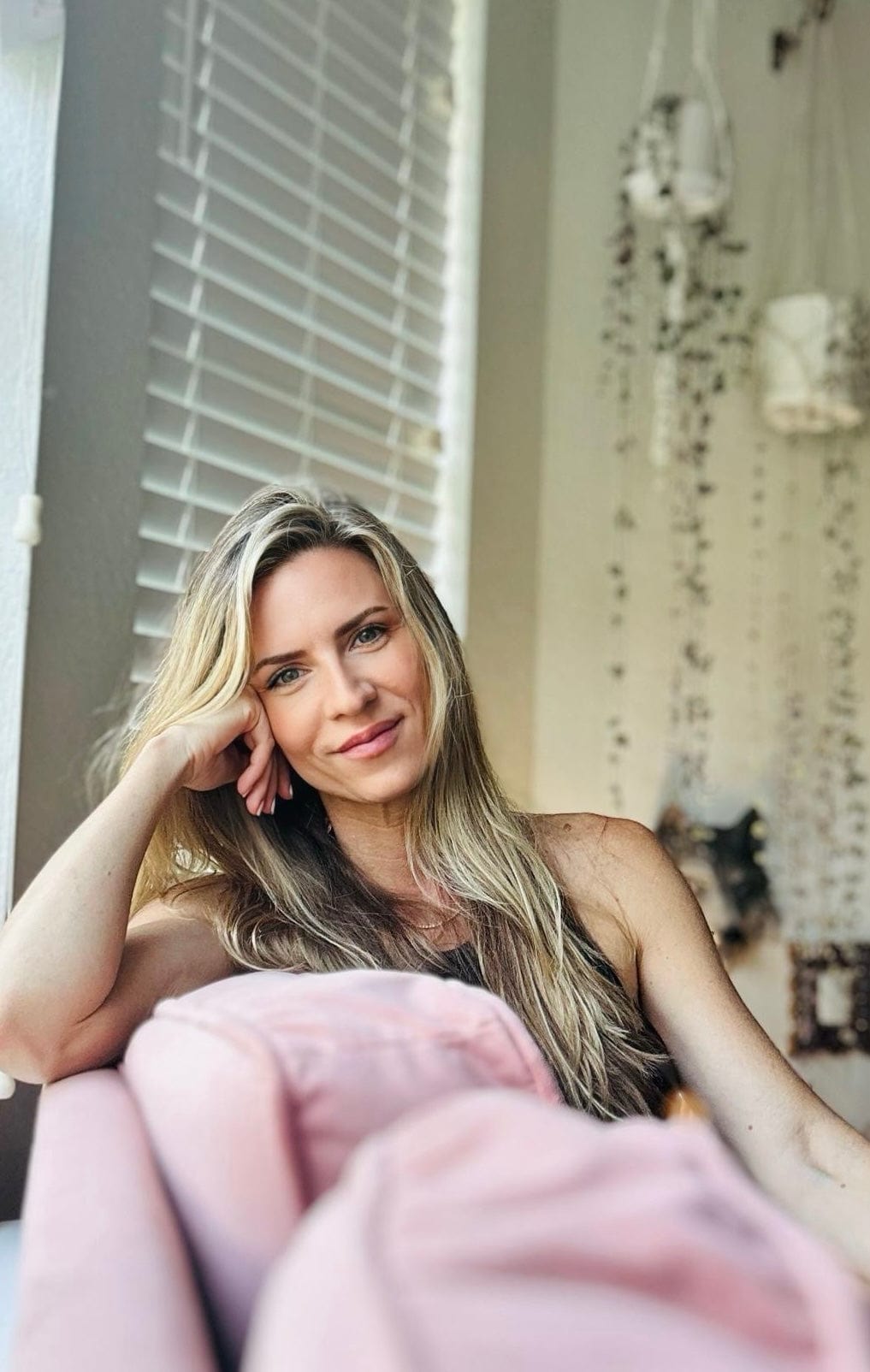 Woman sitting on a couch with a pink blanket, indoors. founder of bellavee, Veronica Winther 