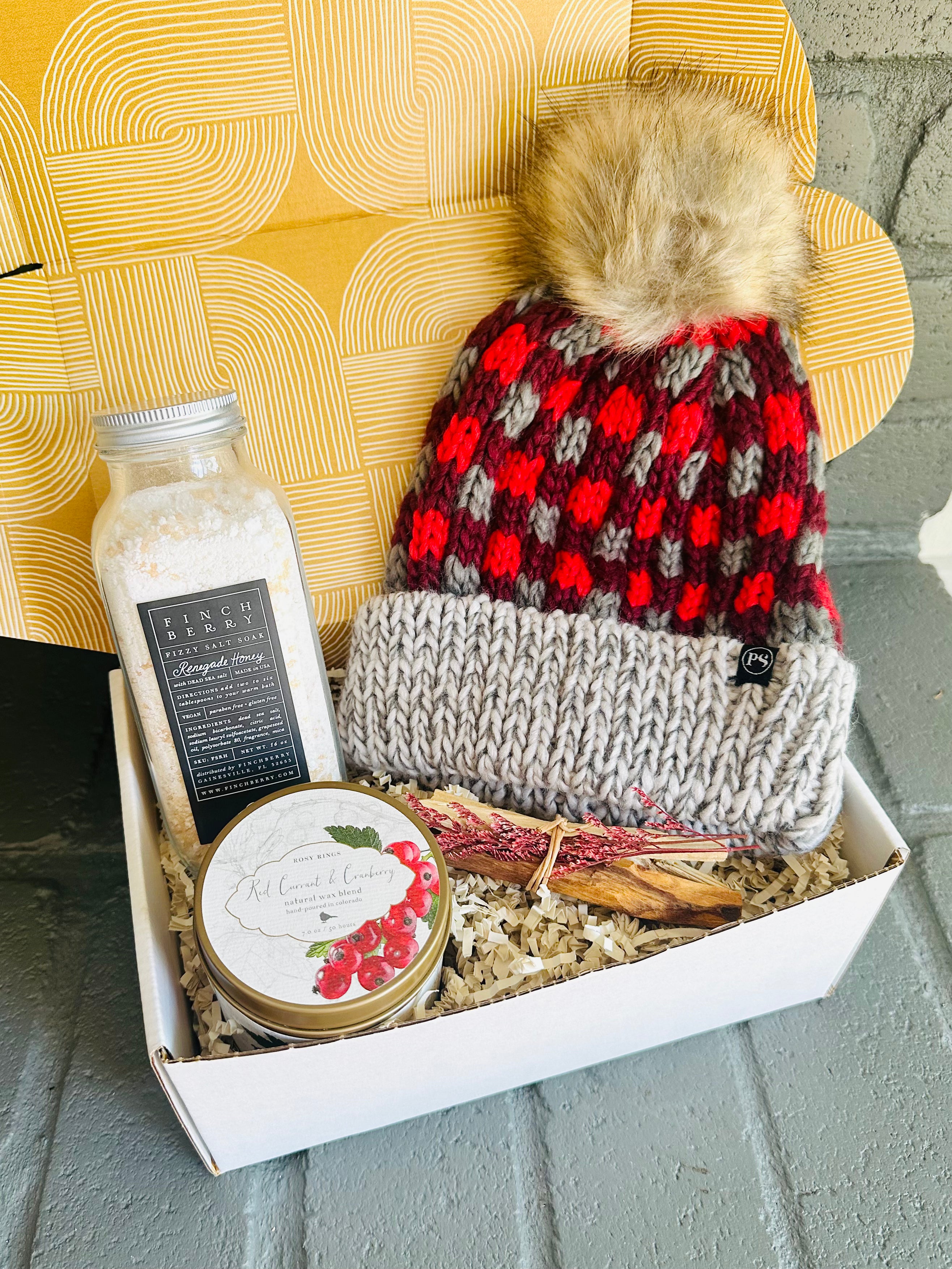 Cozy up with the Holiday Cheer Gift Box, including bath fizzies, Palo Santo, red currant candle, and a red plaid beanie